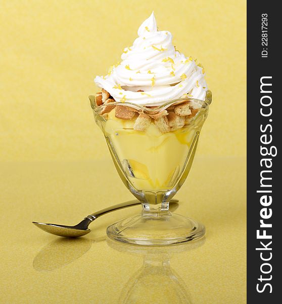 Lemon pudding topped with whipped cream in a glass dish on yellow background