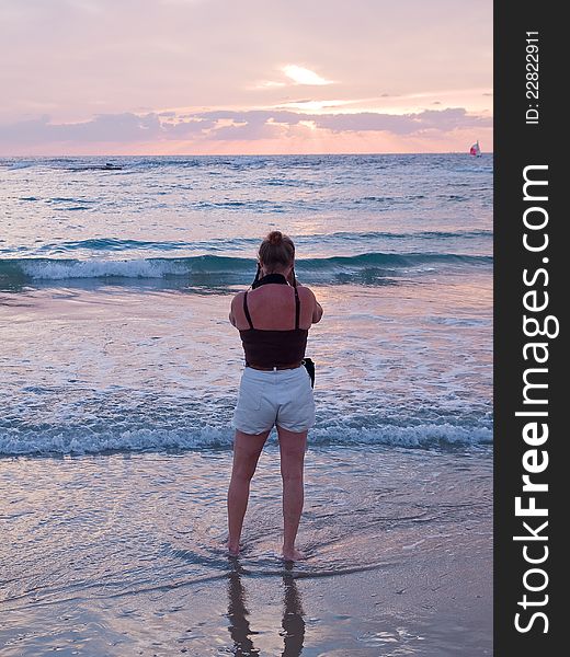 Attractive woman on a beach taking pictures with camera facing beautiful seascape sunset