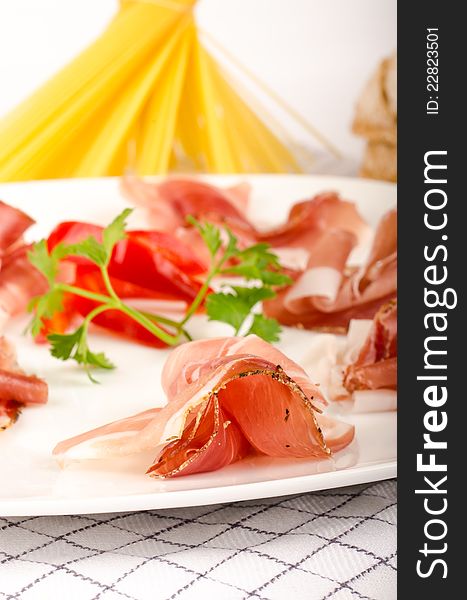 Italian prosciutto appetizer detail on a plate with pasta on the background. Italian prosciutto appetizer detail on a plate with pasta on the background.