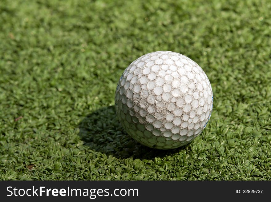 Old scratched dirty golf ball on artificial turf