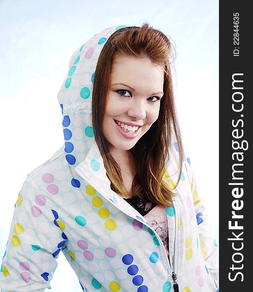 Beautiful smiling brunette woman is ready for April Showers in bright blue and yellow polka dot raincoat. Slight blue sky at top of image. Beautiful smiling brunette woman is ready for April Showers in bright blue and yellow polka dot raincoat. Slight blue sky at top of image.