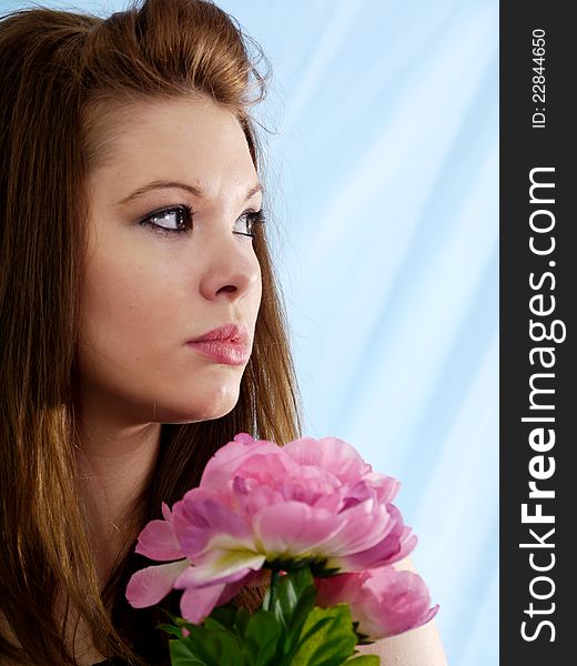 Beautiful brunette woman with romantic expression looking up slightly with pink and green flowers.  Textured sky blue background. Beautiful brunette woman with romantic expression looking up slightly with pink and green flowers.  Textured sky blue background