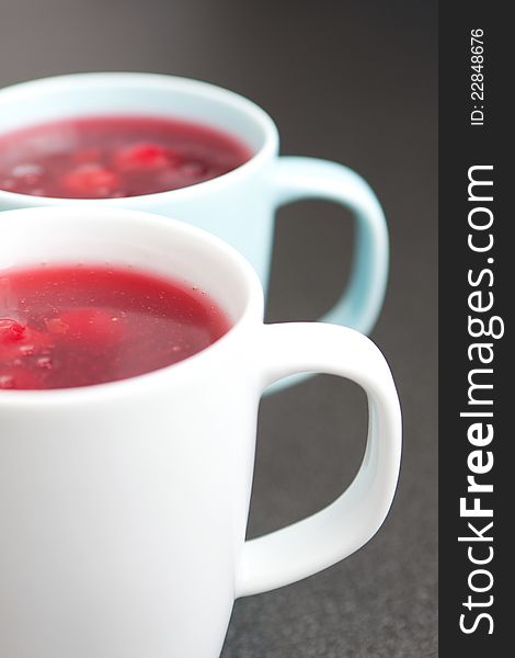 Two white ceramic mugs of fresh red fruit juice with fruit chunks, healthy eating