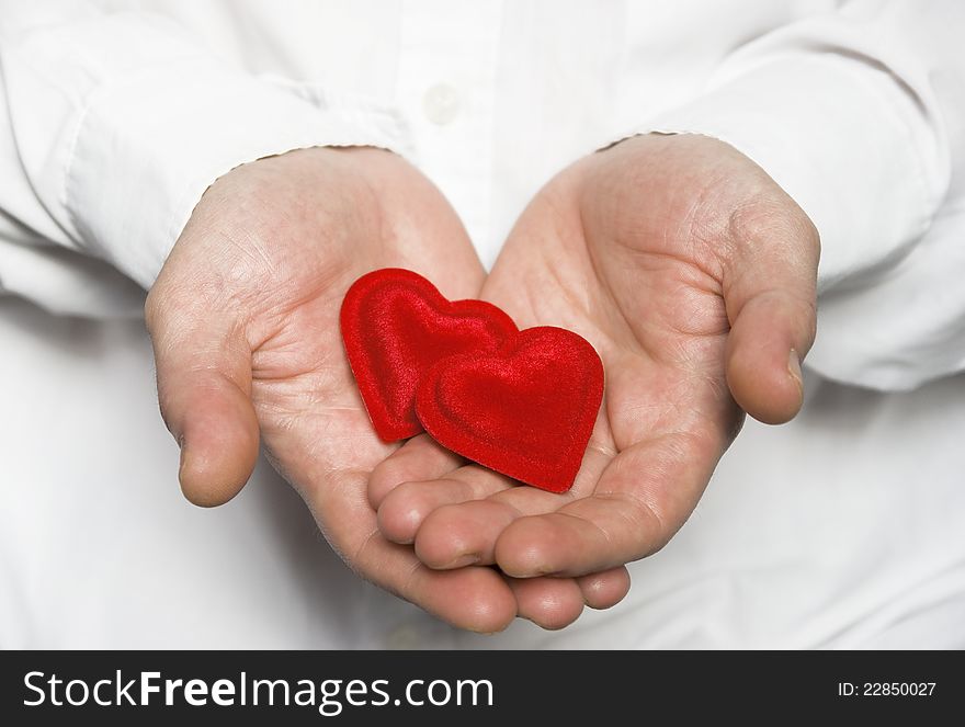Male hand holding two small red hearts with the gesture of offering. Male hand holding two small red hearts with the gesture of offering.