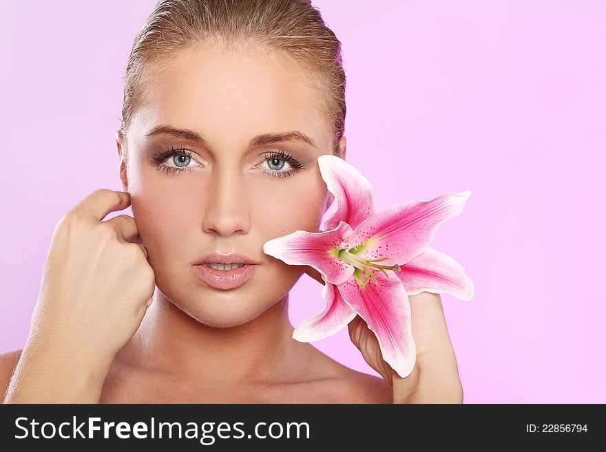 Young and beautiful woman with lily flower over pink background