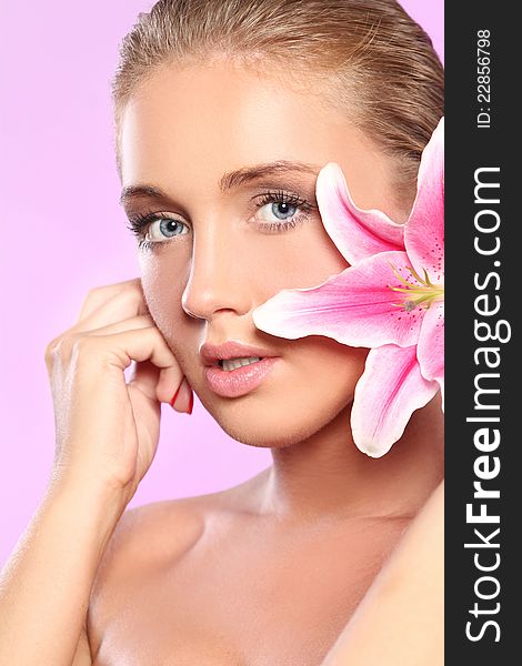 Young and beautiful woman with lily flower over pink background