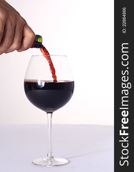 Human hand pouring red wine, white background