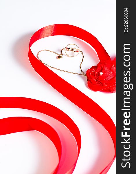 Golden wedding bands and chain with heart surrounded by red ribbon with rose bow on white background. Golden wedding bands and chain with heart surrounded by red ribbon with rose bow on white background