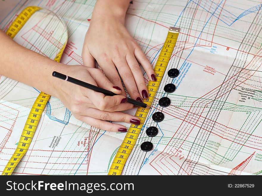 Female hands measuring distance with measuring tape and pencil on sewing pattern