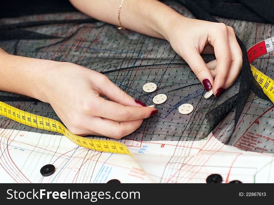Female hands choosing buttons  on cloth over sewing pattern