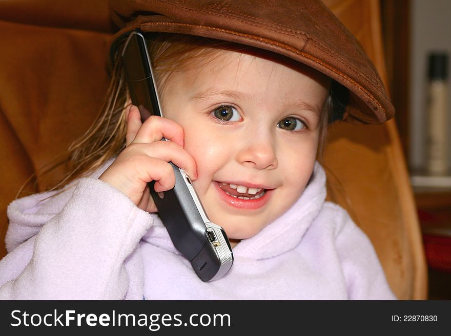 A young toddler speaking on a cell phone wearing a sports cap. A young toddler speaking on a cell phone wearing a sports cap