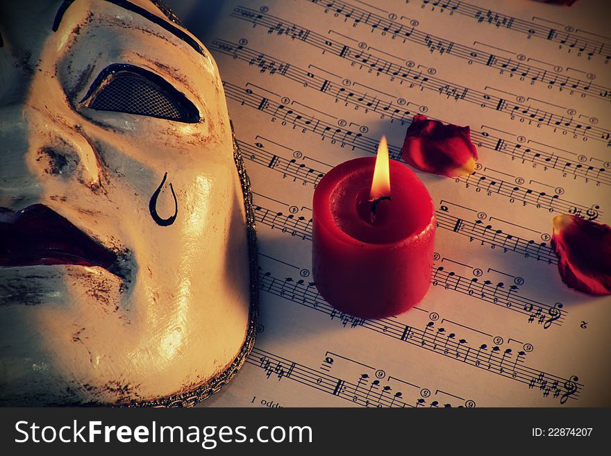 Pierrot mask over music score with lighted candle . Retro styled. Pierrot mask over music score with lighted candle . Retro styled