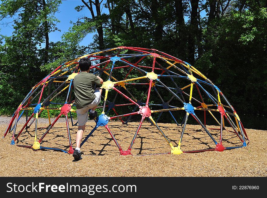 A little boy is trying to climb a colorful structure in a playground. A little boy is trying to climb a colorful structure in a playground