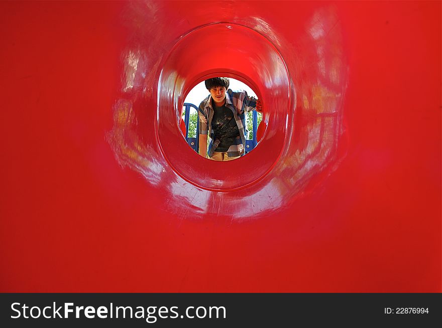 A boy is exploring a red tunnel in a playground.