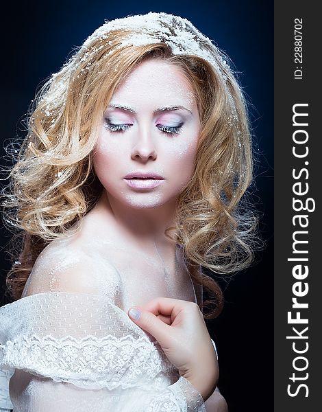 The beautiful blond girl with a winter make-up in a white attire on a dark blue background