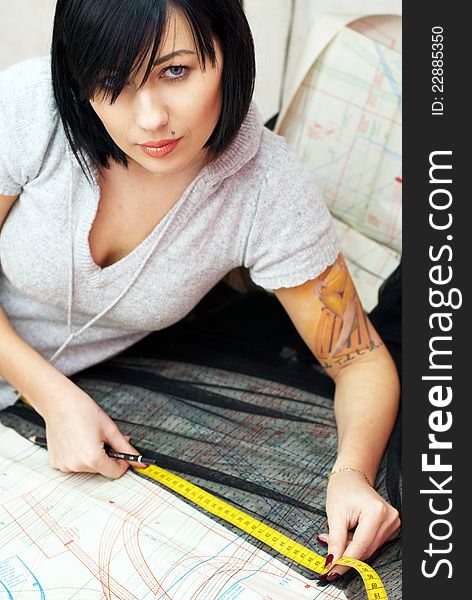 Young seamstress with tattoo measuring distance on sewing pattern with tape and pencil. Young seamstress with tattoo measuring distance on sewing pattern with tape and pencil