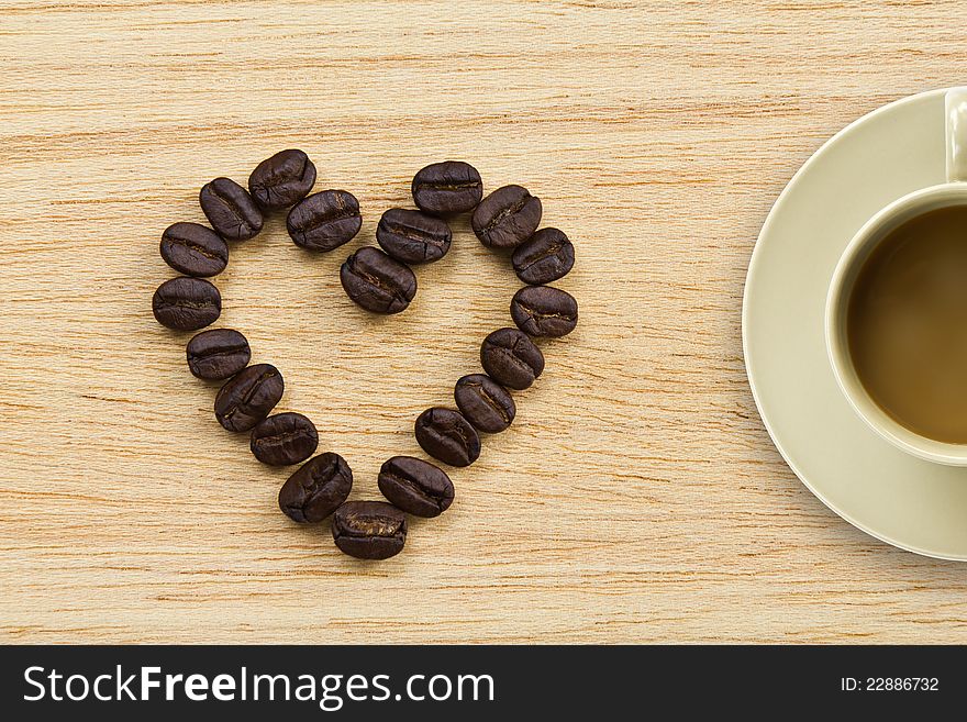 Coffee beans in the form of heart on wooden texture and a cup of coffee. Coffee beans in the form of heart on wooden texture and a cup of coffee