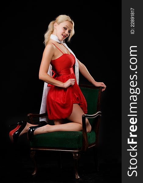 Tender blonde in red dress, white scarf and high heeled shoes posing on chair in the studio, . Tender blonde in red dress, white scarf and high heeled shoes posing on chair in the studio,