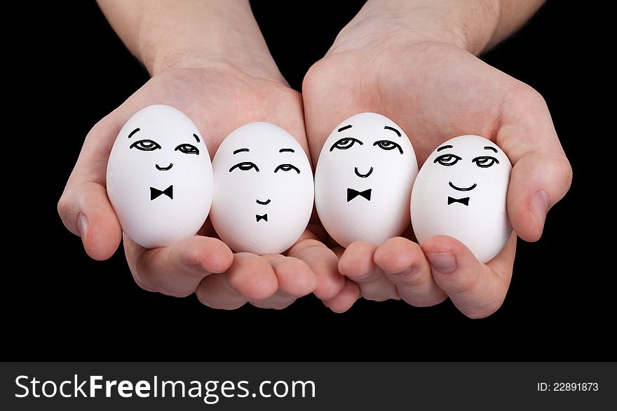 Hand holding cute eggs with funny face smileys on black background