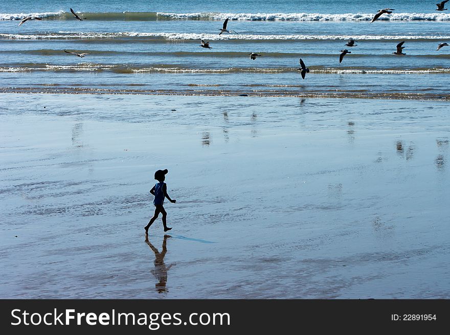 A silhouette of a boy running on the beach towards waves and birds. A silhouette of a boy running on the beach towards waves and birds