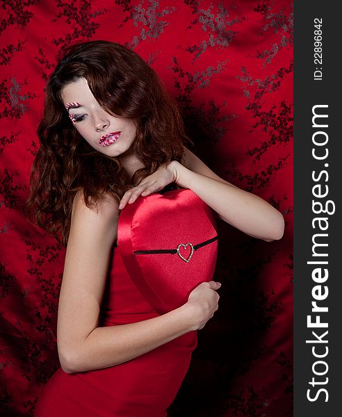 Sexy woman with candy makeup  in a red dress holding a heart shaped present. Sexy woman with candy makeup  in a red dress holding a heart shaped present