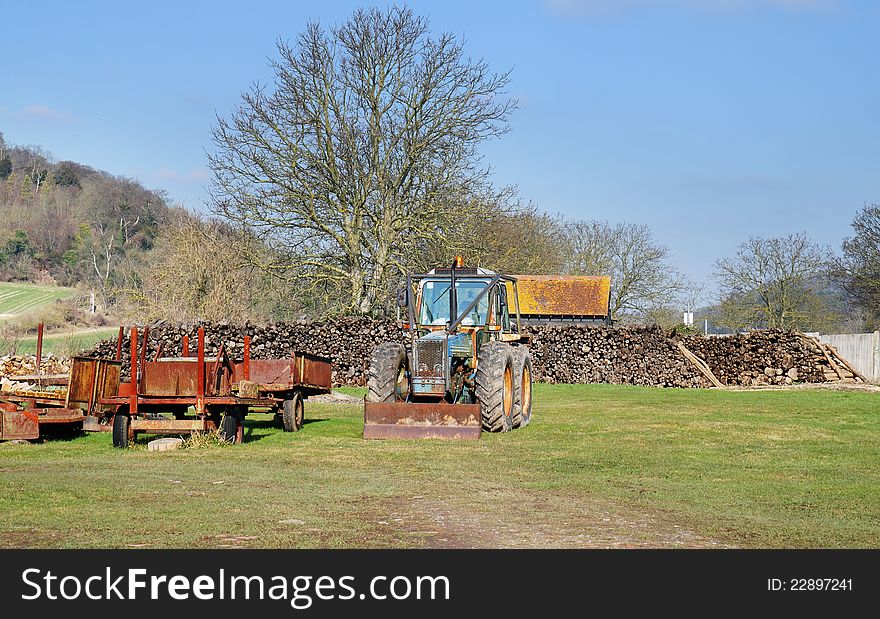 Piles of Timber stacked in a field with Tractor and rusting trailer. Piles of Timber stacked in a field with Tractor and rusting trailer