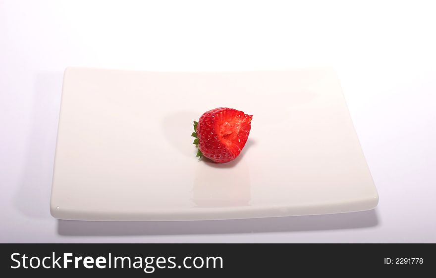 A half-bitten strawberry on a white plate against a white background