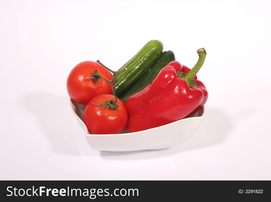 Tomatoes, cucumbers and a red bell pepper in a white bowl against a white background. Tomatoes, cucumbers and a red bell pepper in a white bowl against a white background