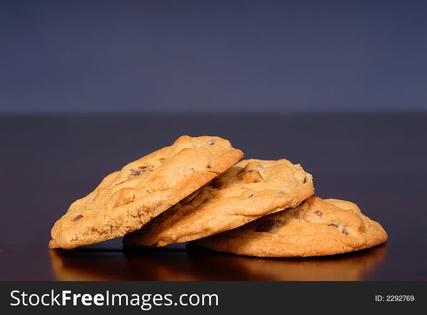Three chocolate chip cookies stacked on table with blue background