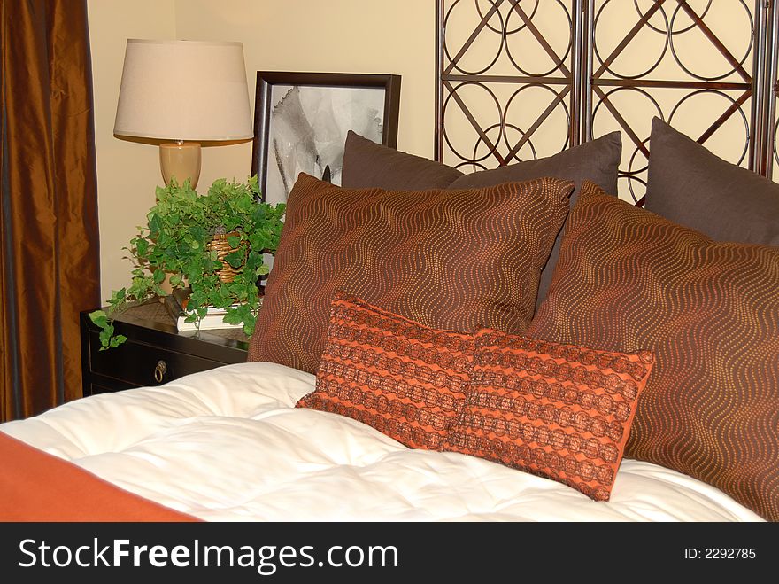 Comfortable bed with earth tone pillows and nightstand. Comfortable bed with earth tone pillows and nightstand