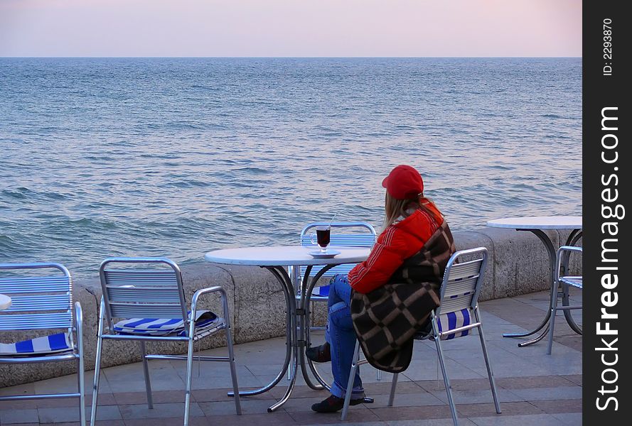 The girl sitting on quay of Black sea with a glass mulled wine