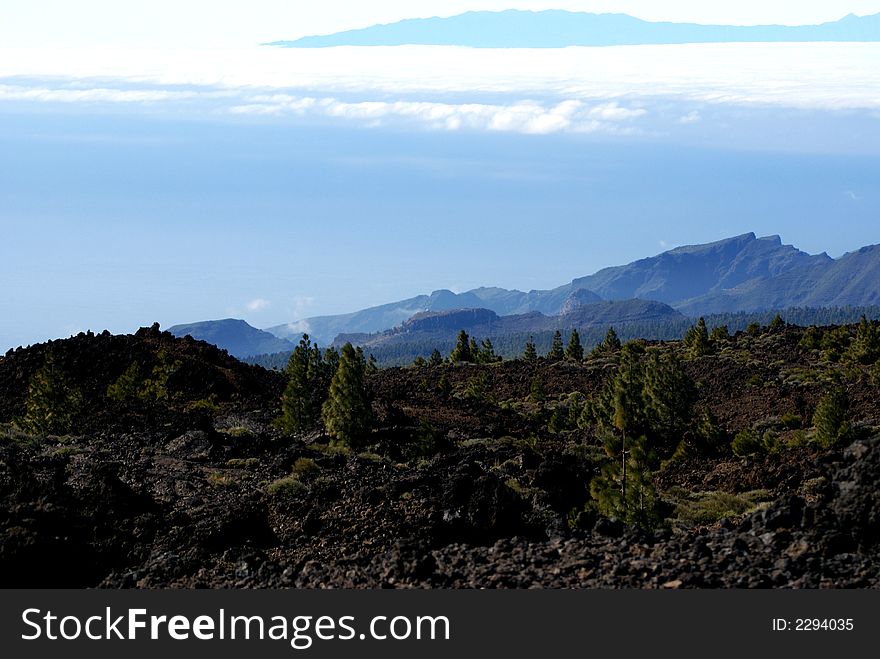 Looking through volcanic rock on top of Mt. Teide giving a perspective of La Gomera being above the floating clouds above the Atlantic. The elevation on the volcano provides a different perspective on the other Canary Islands. Looking through volcanic rock on top of Mt. Teide giving a perspective of La Gomera being above the floating clouds above the Atlantic. The elevation on the volcano provides a different perspective on the other Canary Islands.