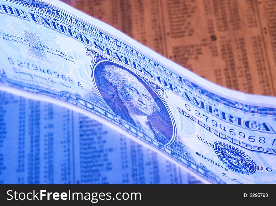 A dollar photographed with orange and blue lighting on a stock report. A dollar photographed with orange and blue lighting on a stock report.