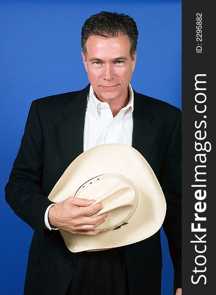 Mature, handsome, white male wearing a black suite and a white shirt holding a cowboy hat with one hand. Mature, handsome, white male wearing a black suite and a white shirt holding a cowboy hat with one hand.