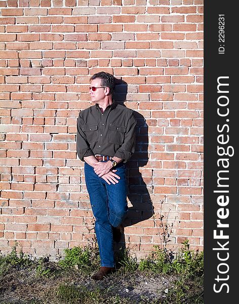 Handsome white male in sunglasses leaning against an old brick wall in the late afternoon as if waiting for someone or something. Handsome white male in sunglasses leaning against an old brick wall in the late afternoon as if waiting for someone or something
