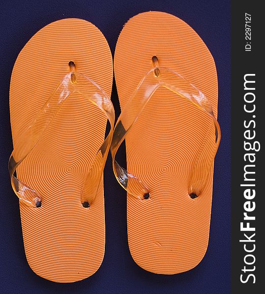 Orange Flipflops against blue background.