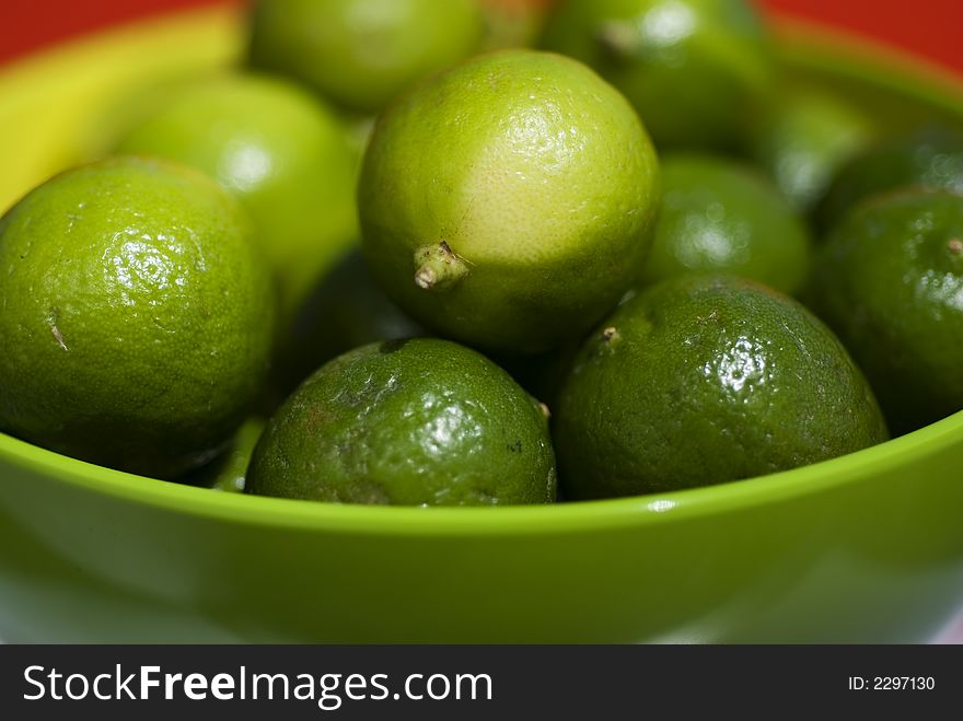 Limes up close in a green bowel against red background.