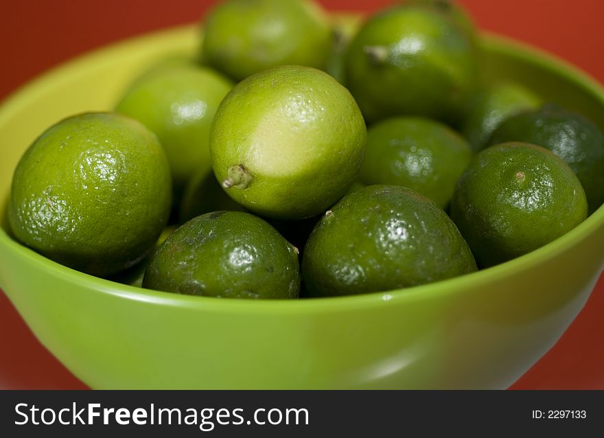 Limes up close in a green bowel against red background.