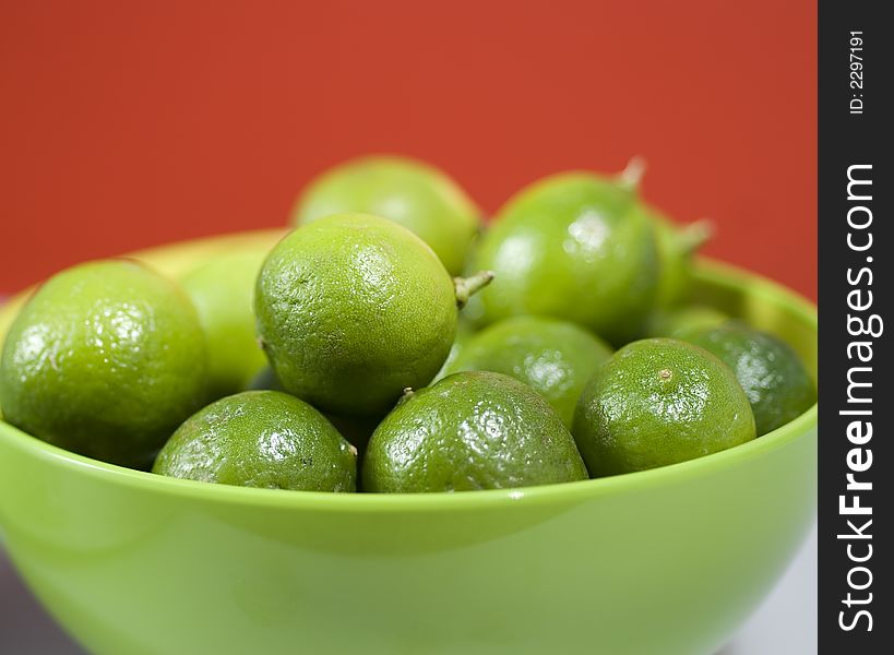 Limes up close in a green bowel against red background.