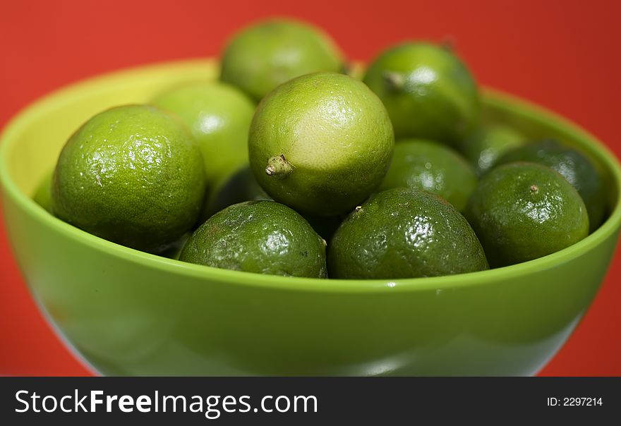 Limes up close in a green bowel against red background.