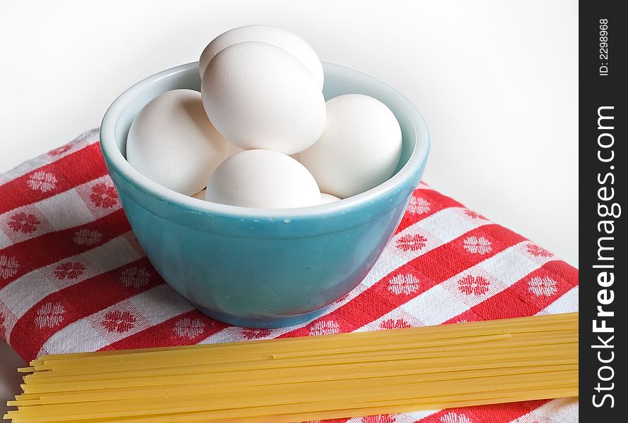 A blue bowl of eggs on red and white tablecloth - pasta in foreground. A blue bowl of eggs on red and white tablecloth - pasta in foreground.