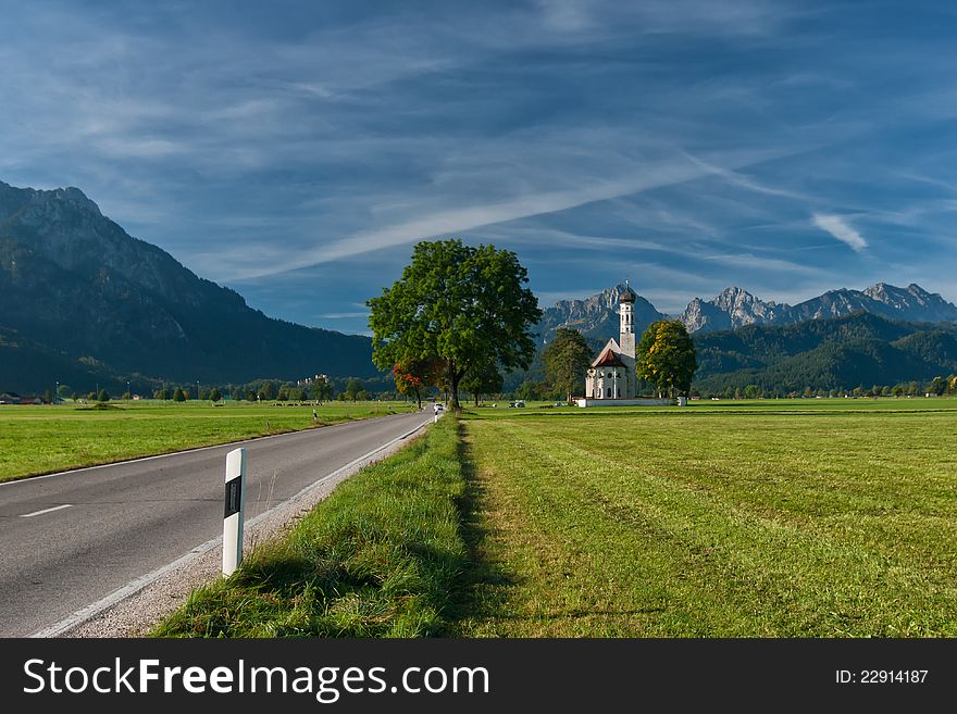 Autumn landscape with road, tree, church, mountains and sky on backgruond