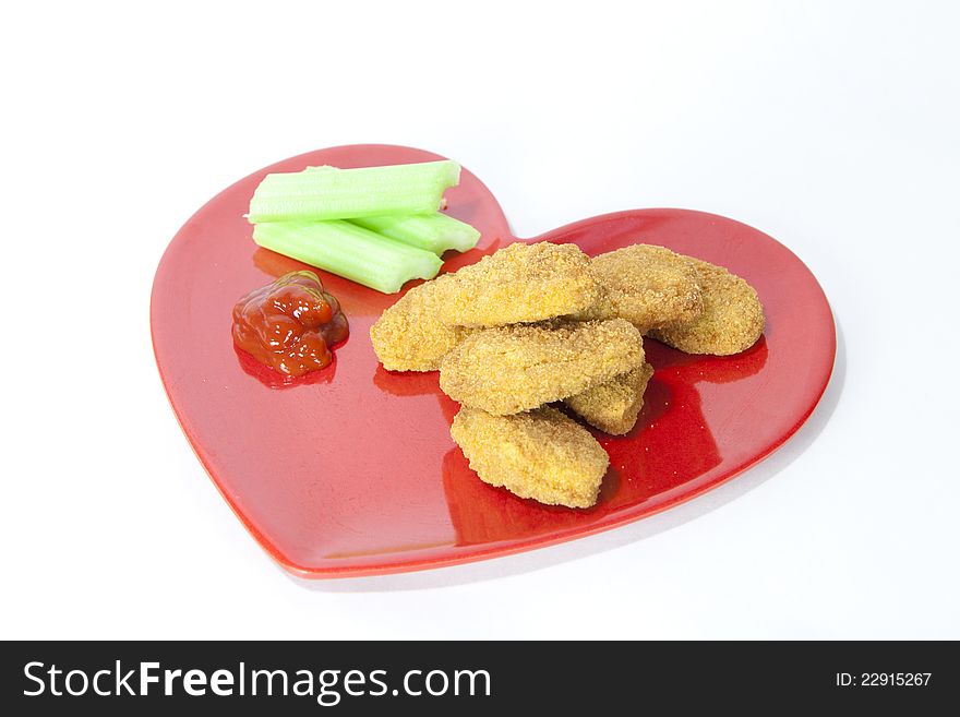 Baked chicken nuggets with sellery and ketchup on red plate in heart shape.