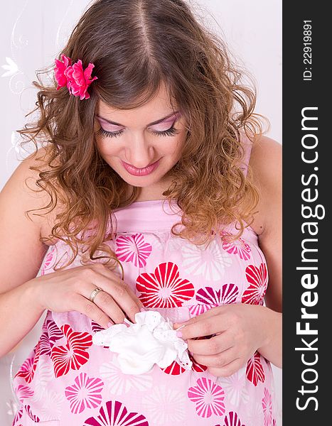 Beautiful pregnant girl with wavy hair wearing pink dress holding baby socks. Beautiful pregnant girl with wavy hair wearing pink dress holding baby socks