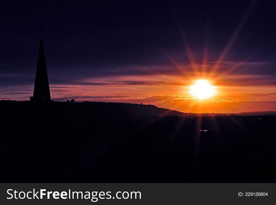 A bright and colourfuol sunset decorates the sky as a church steeple lines the foreground. A bright and colourfuol sunset decorates the sky as a church steeple lines the foreground