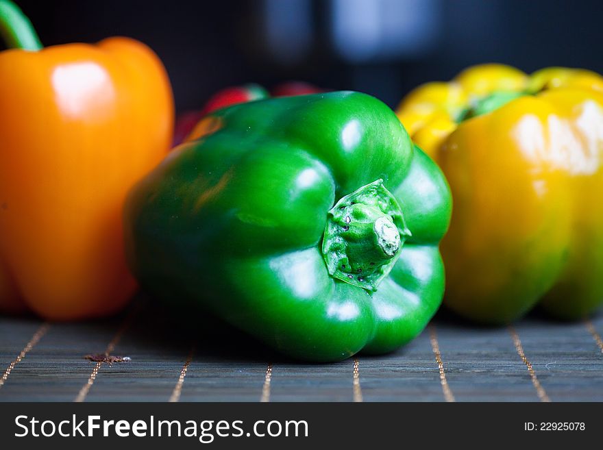 Orange and green sweet pepper in a row on a wooden plate