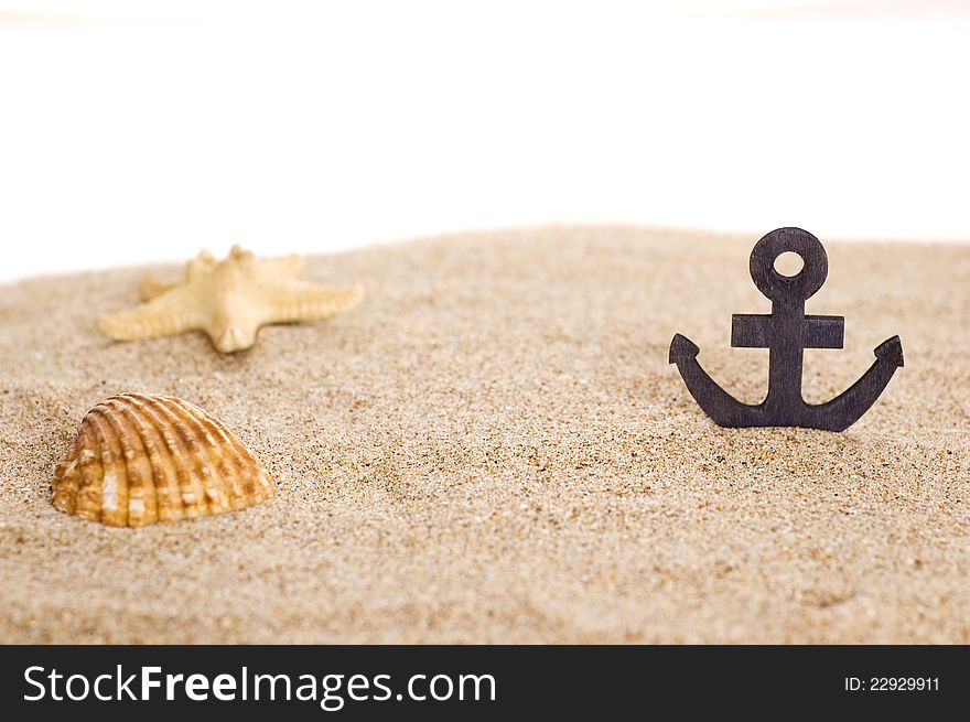 Toylike anchor and seashells on sand isoalted on white background