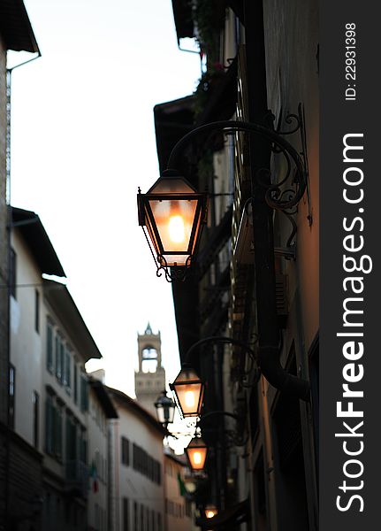 Evening street in Florence. Few glowing vintage street lamps on background with buildings and tower