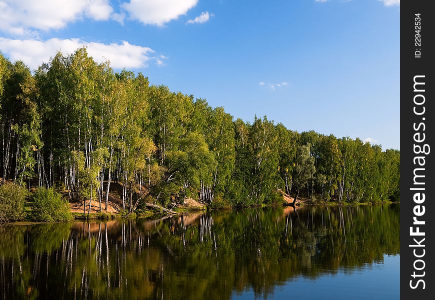 Trees and clouds are reflected in lake in the afternoon. Trees and clouds are reflected in lake in the afternoon.