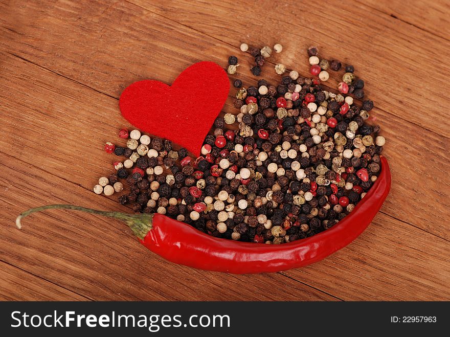 Shape of red heart with red hot chilli pepper and some pile of grounds over wooden background on concept theme of love